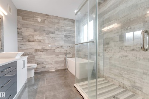 Contemporary bathroom featuring a freestanding soaking tub, glass-enclosed shower with tiled base, dual vanity with vessel sinks, and wood-finish accent wall - 3736 1 Avenue Sw, Edmonton, AB - Indoor Photo Showing Bathroom