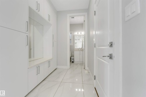 Hallway featuring extensive built-in cabinetry with modern hardware, a recessed mirror, and a light-toned countertop - 3736 1 Avenue Sw, Edmonton, AB - Indoor