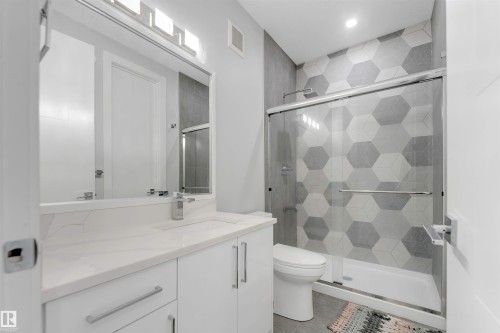 Contemporary bathroom featuring a spacious vanity with a white countertop and rectangular sink, polished chrome faucet, and integrated mirror with overhead lighting - 3736 1 Avenue Sw, Edmonton, AB - Indoor Photo Showing Bathroom