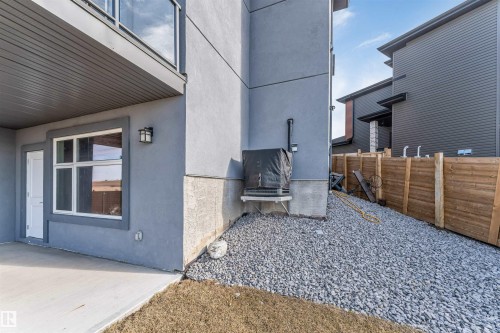 Lower-level concrete patio beneath a covered balcony, featuring an exterior door and a large window - 3736 1 Avenue Sw, Edmonton, AB - Outdoor With Exterior