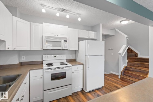 Kitchen featuring white cabinetry, white appliances, laminate countertops, and wood-finish flooring - 5407 204 Street, Edmonton, AB - Indoor Photo Showing Kitchen With Double Sink