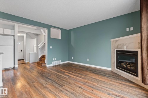 Living space featuring wood-finish flooring, a built-in corner fireplace with a tile surround and mantel, and painted accent walls - 5407 204 Street, Edmonton, AB - Indoor Photo Showing Other Room With Fireplace