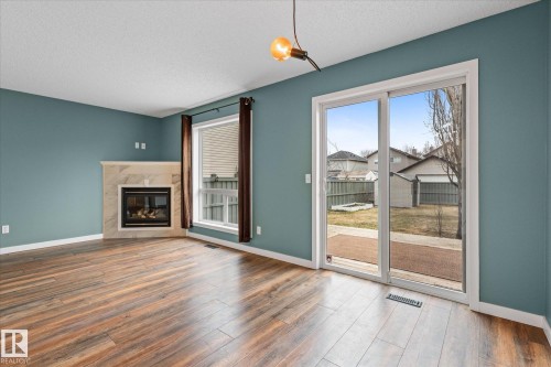 Spacious room featuring wood-finish flooring, a corner fireplace with a tiled surround, and direct outdoor access via sliding glass doors - 5407 204 Street, Edmonton, AB - Indoor Photo Showing Living Room With Fireplace