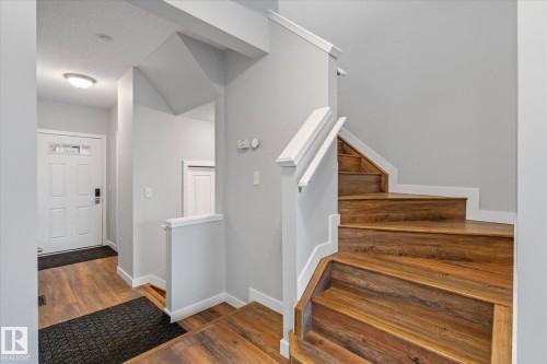 Entryway featuring wood-finish flooring, a white paneled entry door with sidelight, and a staircase with white risers and wood-finish treads - 5407 204 Street, Edmonton, AB - Indoor Photo Showing Other Room