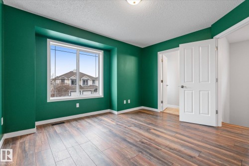 Room featuring wood-finish flooring, a large window, a ceiling-mounted light fixture, white trim, and a four-panel interior door - 5407 204 Street, Edmonton, AB - Indoor Photo Showing Other Room