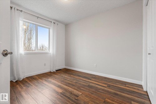 Room featuring wood-finish flooring, a white trim package, and a double-pane window with a neutral sky backdrop - 5407 204 Street, Edmonton, AB - Indoor Photo Showing Other Room