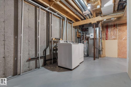 Unfinished basement laundry area featuring a washer and dryer, exposed concrete walls, painted concrete flooring, and visible ceiling joists with utility lines - 5407 204 Street, Edmonton, AB - Indoor