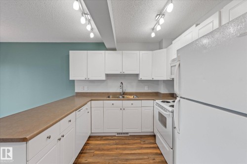 Kitchen featuring white cabinetry and appliances, laminate countertops, wood-finish flooring, and track lighting - 5407 204 Street, Edmonton, AB - Indoor Photo Showing Kitchen With Double Sink