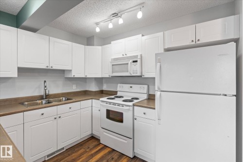 Kitchen featuring white cabinetry, laminate countertops, a double basin stainless steel sink with a gooseneck faucet, a white electric range, and wood-finish flooring - 5407 204 Street, Edmonton, AB - Indoor Photo Showing Kitchen With Double Sink