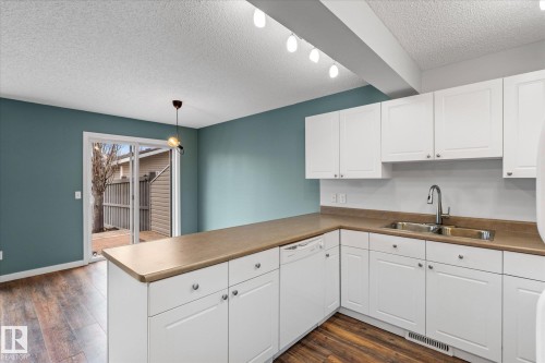Kitchen featuring white shaker cabinetry, stainless steel sink with gooseneck faucet, light brown countertops, and wood-finish flooring - 5407 204 Street, Edmonton, AB - Indoor Photo Showing Kitchen With Double Sink