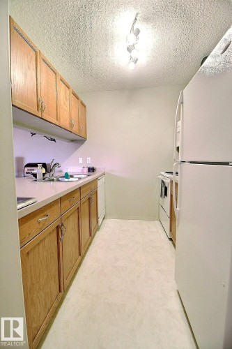 Galley kitchen featuring light wood cabinetry, light countertops, white appliances, and track lighting - 413 279 Suder Greens Drive, Edmonton, AB - Indoor Photo Showing Kitchen