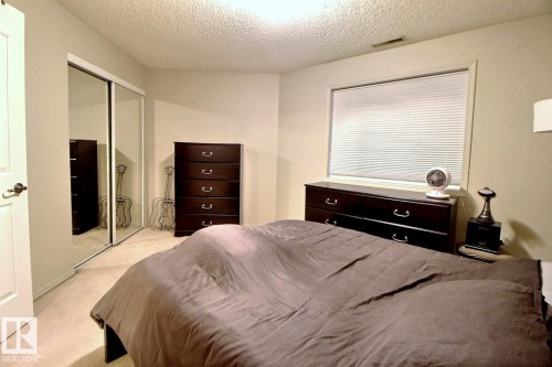 Interior room featuring neutral wall paint, textured ceiling, a window with horizontal blinds, and mirrored sliding closet doors - 413 279 Suder Greens Drive, Edmonton, AB - Indoor Photo Showing Bedroom