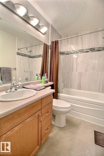 Bathroom featuring a light-toned vanity with an integrated sink, a full-width mirror, and a three-light fixture - 413 279 Suder Greens Drive, Edmonton, AB - Indoor Photo Showing Bathroom