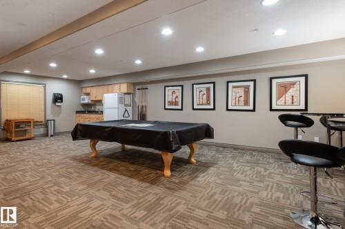 Recreation room featuring patterned carpet flooring and a built-in wet bar with wood cabinetry and a white refrigerator - 413 279 Suder Greens Drive, Edmonton, AB - Indoor Photo Showing Other Room