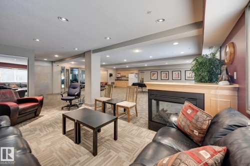 Spacious common area featuring a built-in fireplace with a wood mantel, recessed lighting, and patterned carpet tile flooring - 413 279 Suder Greens Drive, Edmonton, AB - Indoor Photo Showing Living Room With Fireplace