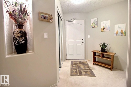 Entryway featuring a paneled door, light-colored carpeting, a wall niche with accent lighting, and a mirrored closet door - 413 279 Suder Greens Drive, Edmonton, AB - Indoor Photo Showing Other Room