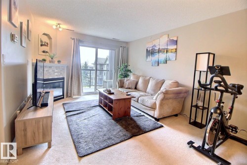 Living area with a corner fireplace featuring a stacked stone surround and white mantel - 413 279 Suder Greens Drive, Edmonton, AB - Indoor Photo Showing Living Room With Fireplace