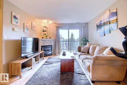 Living area featuring a corner fireplace with a tile surround and mantel, sliding glass door to a balcony, carpeting, and light-toned walls - 413 279 Suder Greens Drive, Edmonton, AB - Indoor Photo Showing Living Room With Fireplace