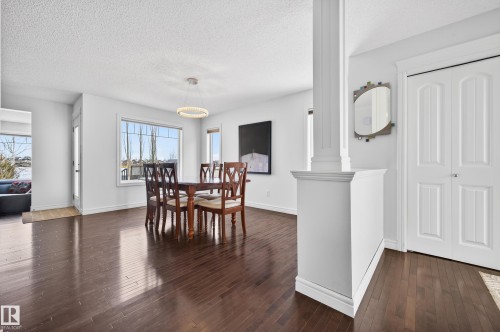 Spacious dining area featuring dark wood-finish flooring, a contemporary chandelier, large windows providing natural light, white trim, and a decorative column - 8477 Sloane Crescent, Edmonton, AB - Indoor Photo Showing Dining Room