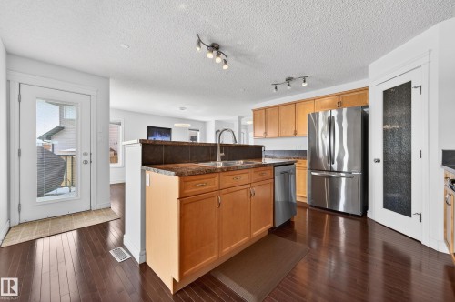 Kitchen featuring wood-finish flooring, light wood cabinetry, stainless steel appliances, a double basin sink, and track lighting - 8477 Sloane Crescent, Edmonton, AB - Indoor Photo Showing Kitchen With Double Sink