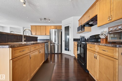 Kitchen featuring wood cabinetry, dark countertops, and stainless steel appliances - 8477 Sloane Crescent, Edmonton, AB - Indoor Photo Showing Kitchen