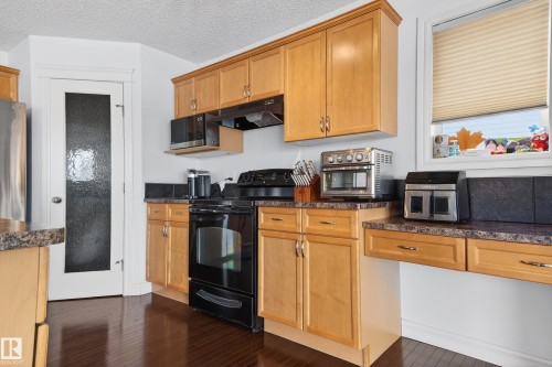 Kitchen featuring wood-finish flooring, light wood cabinetry, stone-look countertops, and a full suite of black appliances - 8477 Sloane Crescent, Edmonton, AB - Indoor Photo Showing Kitchen