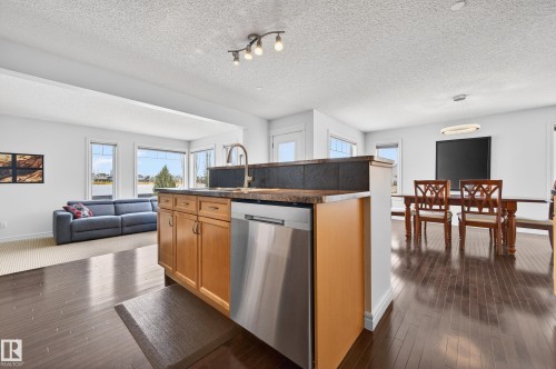Kitchen island featuring light wood cabinetry, stainless steel dishwasher, and a dark countertop - 8477 Sloane Crescent, Edmonton, AB - Indoor Photo Showing Other Room
