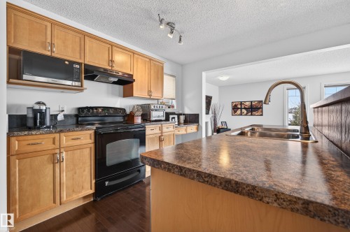 Kitchen featuring light wood-finish cabinetry, dark countertops, a built-in microwave, and a black range - 8477 Sloane Crescent, Edmonton, AB - Indoor Photo Showing Kitchen
