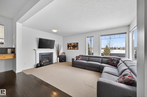 Living area featuring a fireplace with a white mantel, large windows, and a built-in counter with a granite-style countertop - 8477 Sloane Crescent, Edmonton, AB - Indoor Photo Showing Living Room With Fireplace
