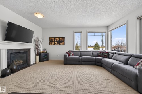 Spacious living area featuring a central fireplace with a white mantel and dark tile surround - 8477 Sloane Crescent, Edmonton, AB - Indoor Photo Showing Living Room With Fireplace