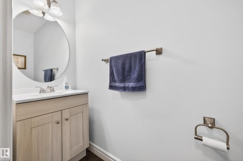 Bathroom vanity featuring a light wood-finish cabinet with double doors, a white countertop, and a circular mirror - 8477 Sloane Crescent, Edmonton, AB - Indoor Photo Showing Bathroom