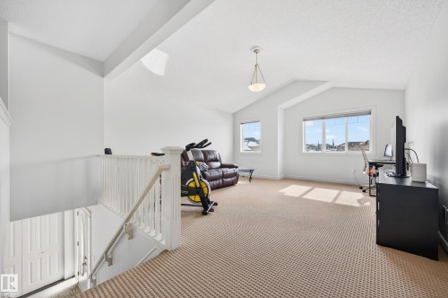 Carpeted upper-level space featuring a contemporary pendant light fixture, multiple windows, and vaulted ceilings - 8477 Sloane Crescent, Edmonton, AB - Indoor