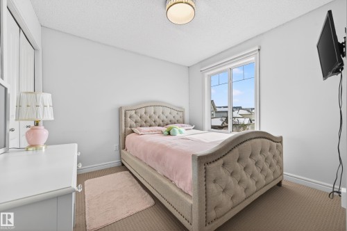 Bedroom featuring a large window, neutral carpeting, light-colored walls, and a built-in closet with white bifold doors - 8477 Sloane Crescent, Edmonton, AB - Indoor Photo Showing Bedroom