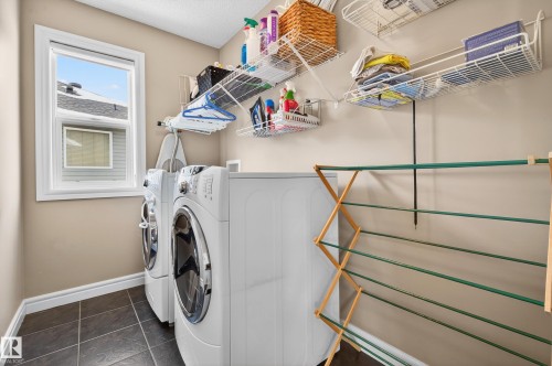 Dedicated laundry space featuring a window, tile flooring, and integrated wall-mounted shelving - 8477 Sloane Crescent, Edmonton, AB - Indoor Photo Showing Laundry Room