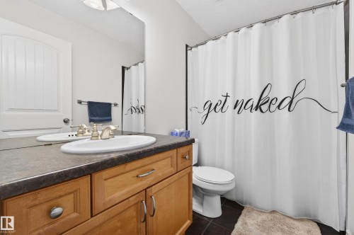 Bathroom featuring a light wood-finish vanity with a drop-in sink and brushed nickel faucet, a dark countertop, and dark tile flooring - 8477 Sloane Crescent, Edmonton, AB - Indoor Photo Showing Bathroom