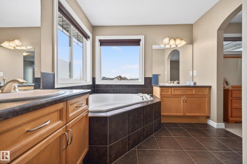 Spacious bathroom featuring an integrated corner tub with tiled surround, dual vanity areas with wood cabinetry and dark countertops, and large windows - 8477 Sloane Crescent, Edmonton, AB - Indoor Photo Showing Bathroom