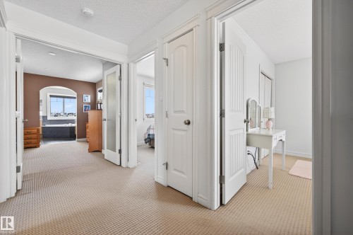 Carpeted hallway providing access to multiple rooms, including a room with a large window and a room with a partial window - 8477 Sloane Crescent, Edmonton, AB - Indoor Photo Showing Other Room