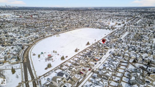 Residential neighborhood featuring a curved street layout, snow-covered rooftops, and a large central park area with recreational equipment - 8477 Sloane Crescent, Edmonton, AB - Outdoor With View