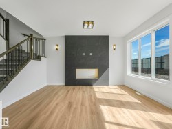 Spacious room featuring wood-finish flooring, a modern black tile fireplace surround with a recessed opening, and large windows providing abundant illumination - 