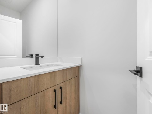 Modern vanity featuring wood-finish cabinetry, a white countertop, an undermount sink, and a matte black faucet - 272 Munn Way, Leduc, AB - Indoor Photo Showing Bathroom