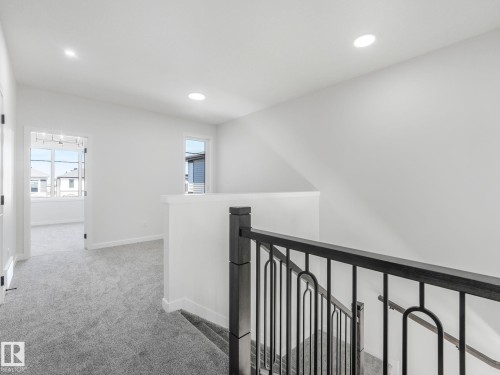 Upper-level landing featuring textured gray carpeting, recessed ceiling lighting, and a dark wood-finish newel post and handrail with wrought iron balusters - 272 Munn Way, Leduc, AB - Indoor Photo Showing Other Room