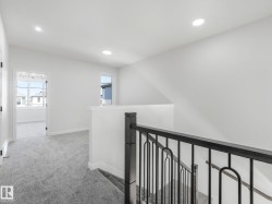 Upper-level landing featuring textured gray carpeting, recessed ceiling lighting, and a dark wood-finish newel post and handrail with wrought iron balusters - 