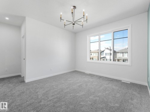 Spacious room featuring gray carpeting, a large multipane window, a contemporary black and gold chandelier, and recessed lighting - 272 Munn Way, Leduc, AB - Indoor Photo Showing Other Room