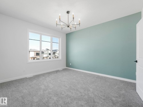Interior room featuring a large multi-pane window, neutral gray carpeting, and a modern chandelier light fixture - 272 Munn Way, Leduc, AB - Indoor Photo Showing Other Room