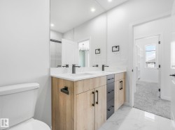 Contemporary bathroom featuring a dual vanity with wood-finish and dark cabinetry, quartz countertops, and matte black fixtures - 