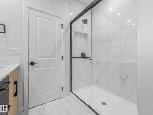 Glass-enclosed shower with matte black hardware, integrated niche shelving, and large format tile surround - 272 Munn Way, Leduc, AB - Indoor Photo Showing Bathroom