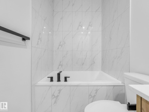 Built-in soaking tub with matte black fixtures, surrounded by large format white marble-look wall tiles - 272 Munn Way, Leduc, AB - Indoor Photo Showing Bathroom