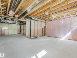 Unfinished basement space featuring exposed wood framing, concrete flooring, visible insulation, and overhead ductwork - 