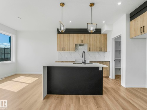 Kitchen featuring a large island with a light-toned countertop, wood-finish flooring, and natural wood cabinetry - 272 Munn Way, Leduc, AB - Indoor Photo Showing Kitchen