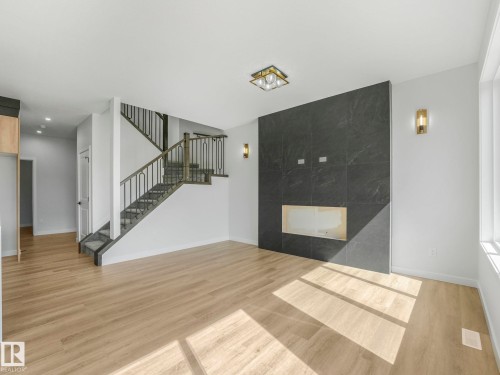 Spacious living area featuring light wood-finish flooring, a contemporary fireplace wall with dark stone-look tiling and a firebox opening, and a detailed staircase with dark wood-finish handrails and black metal balusters - 272 Munn Way, Leduc, AB - Indoor Photo Showing Other Room